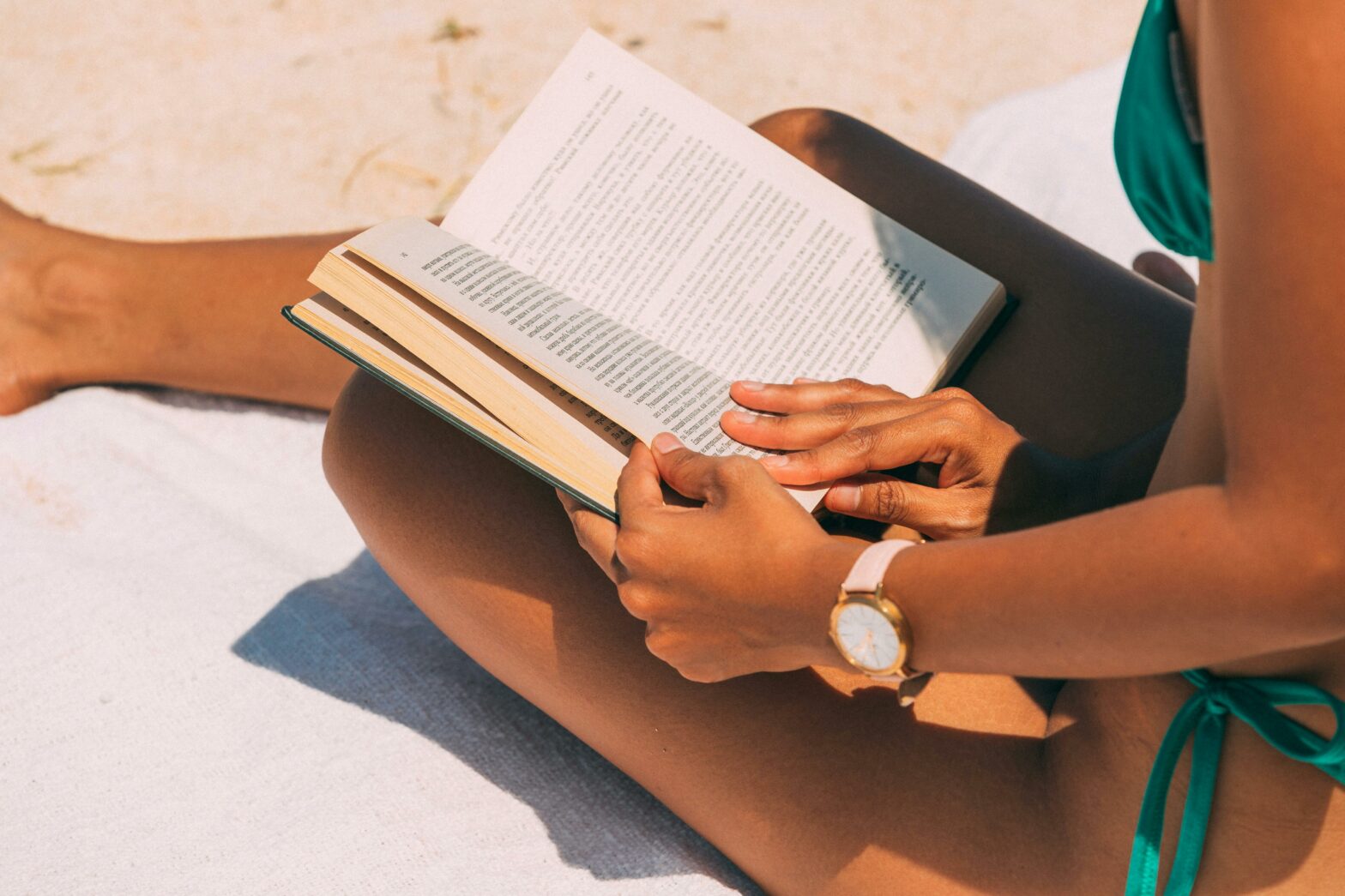 Close-up of a woman reading on a sandy beach in summer sunlight.