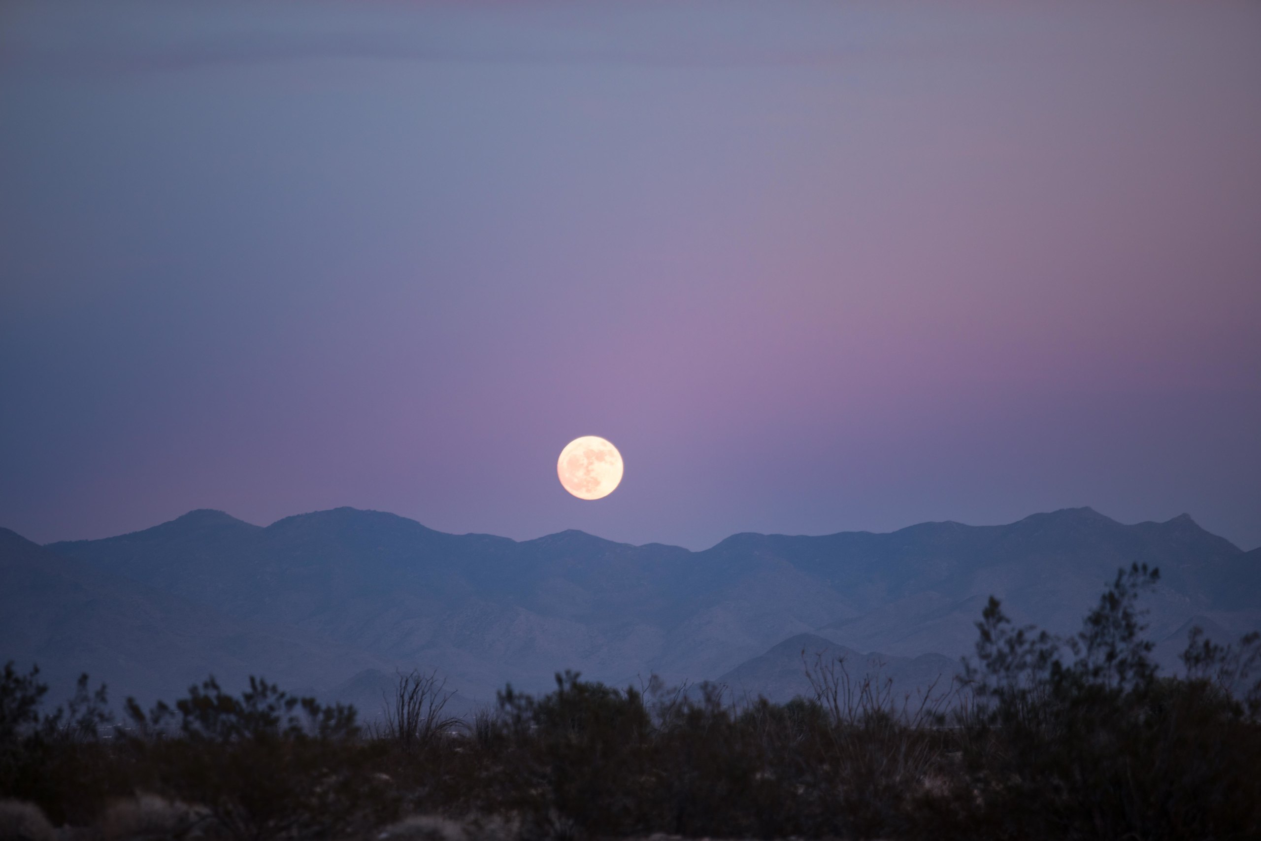 Pleine lune au-dessus de silhouettes de montagnes, ciel du soir rose et mauve