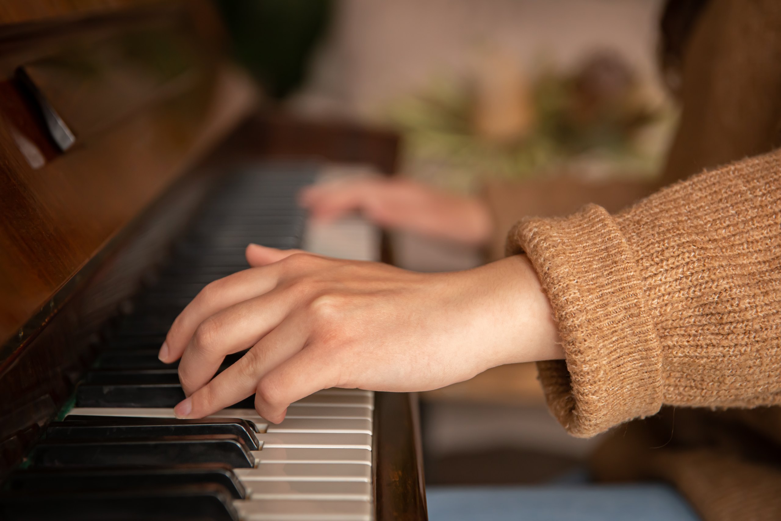 Mains de femme jouant sur un piano ancien, pull beige, gros plan