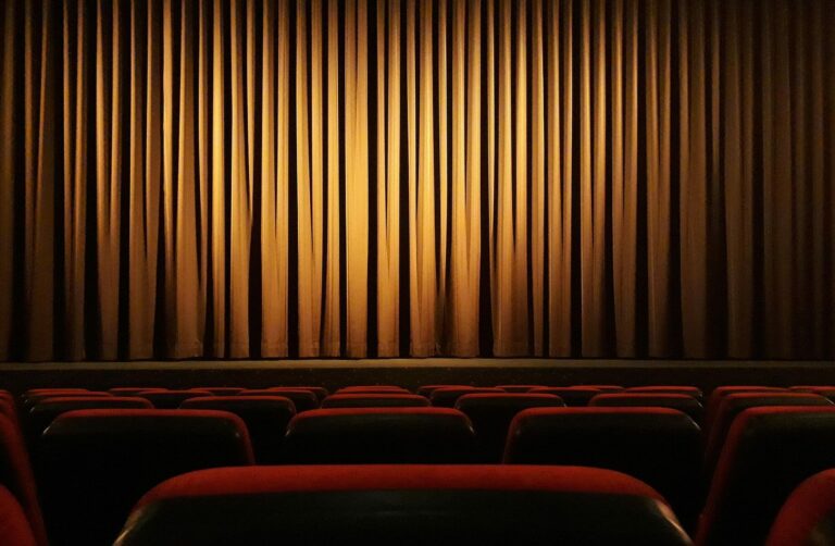 Rideau de scène fermé dans la pénombre d'une salle de cinéma aux fauteuils rouges