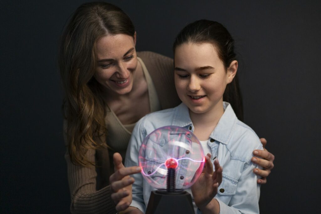 Une femme et une fillette posent les mains sur une boule plasma lumineuse dans une salle sombre