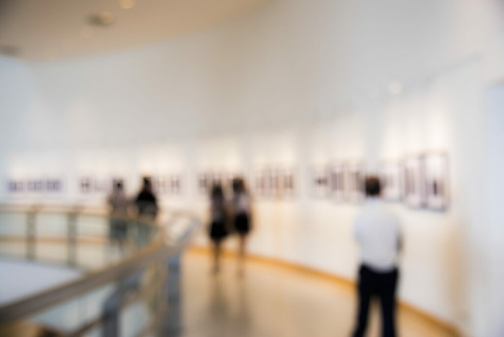Visiteurs flous parcourant une galerie d'exposition lumineuse aux murs blancs