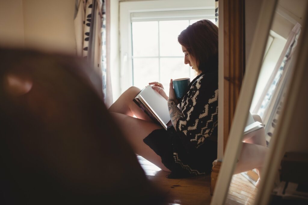 Femme lisant assise près d'une fenêtre, dans la pénombre