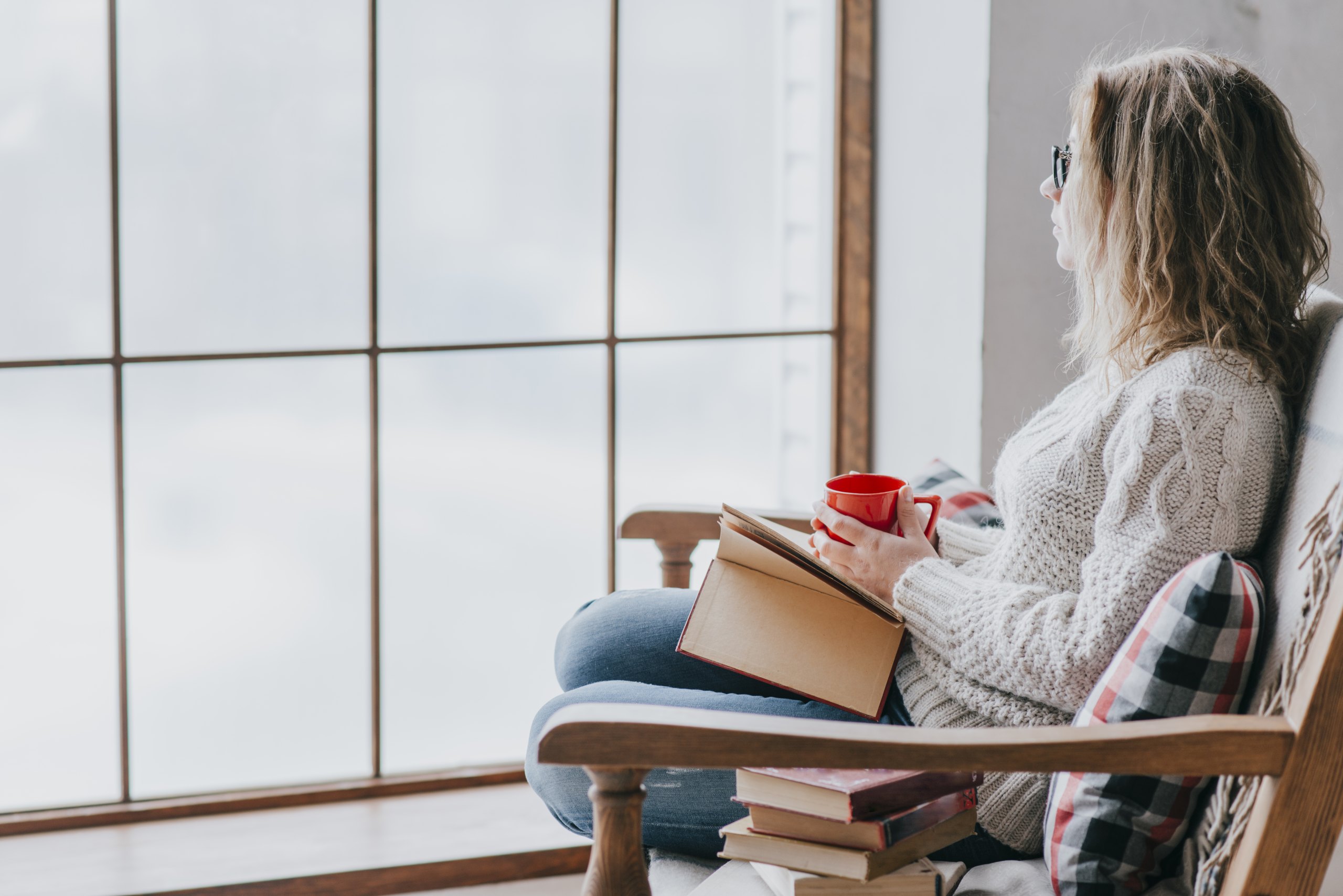 Femme lisant un livre, une tasse à la main, près d'une fenêtre