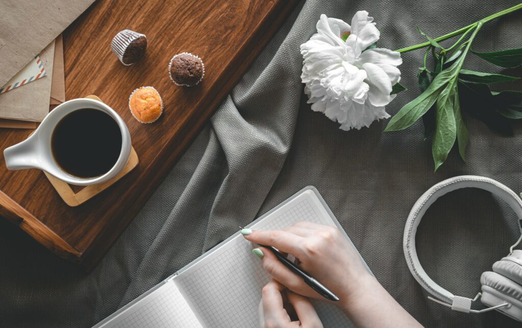 Main écrivant dans un carnet, café et fleurs sur un plateau