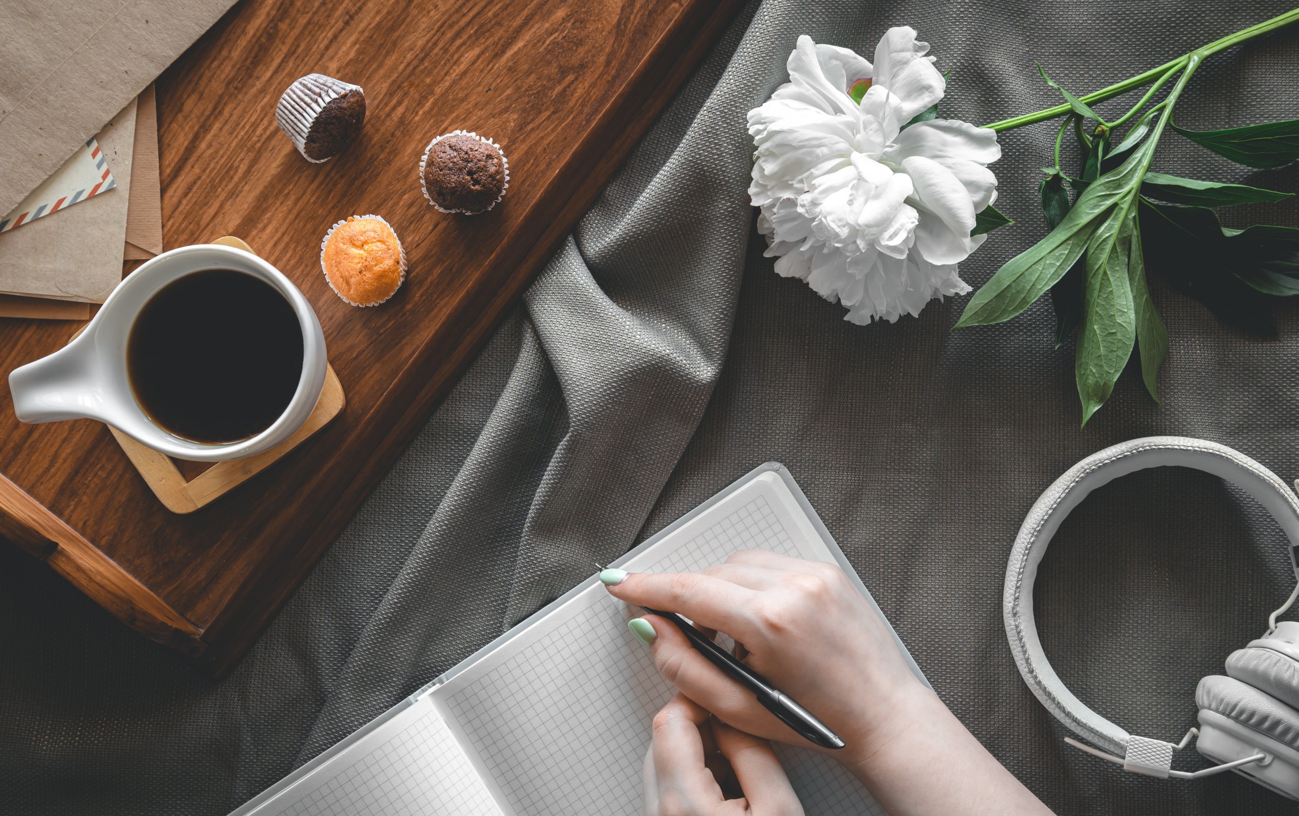 Main écrivant dans un carnet, café et fleurs sur un plateau