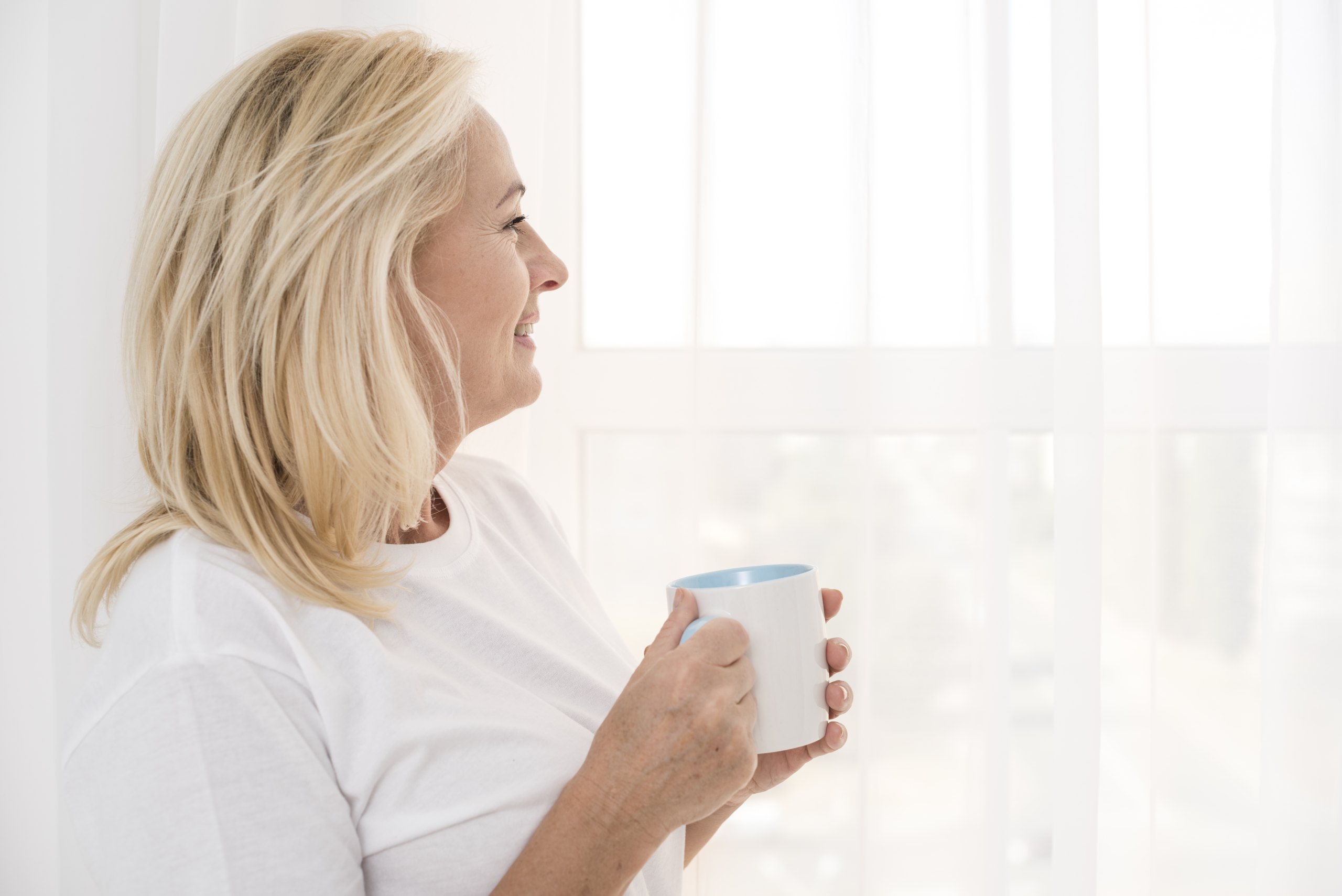 Femme souriante, une tasse à la main, regardant par la fenêtre