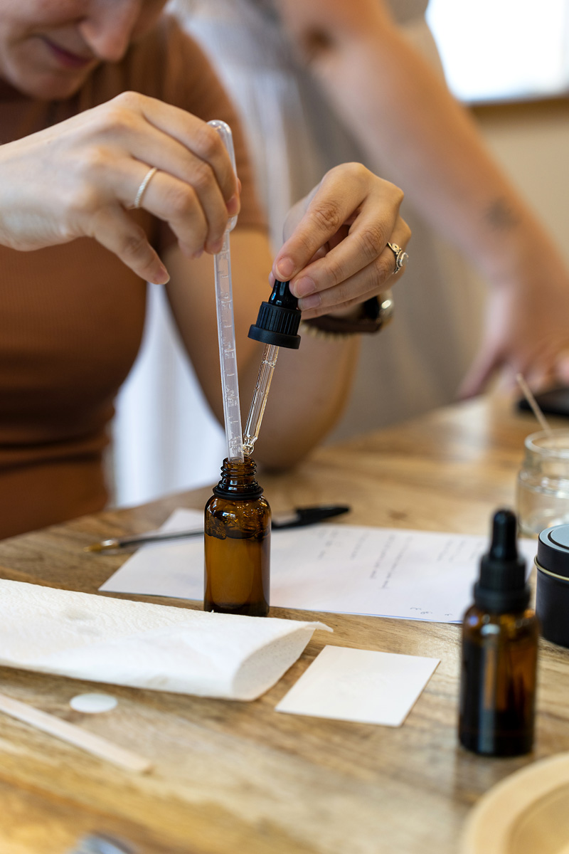 Mains versant quelques gouttes d’essence à la pipette dans un flacon ambré, lors d’un atelier de création de parfum