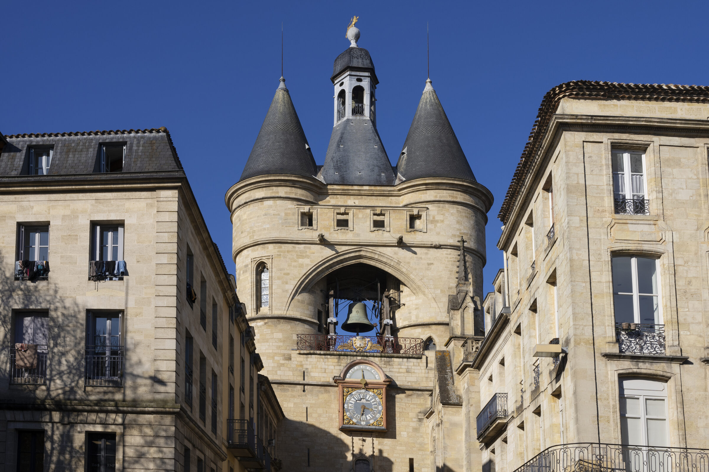 La Grosse Cloche de Bordeaux, porte médiévale aux tours coniques encadrée de façades en pierre blonde, sous un ciel bleu
