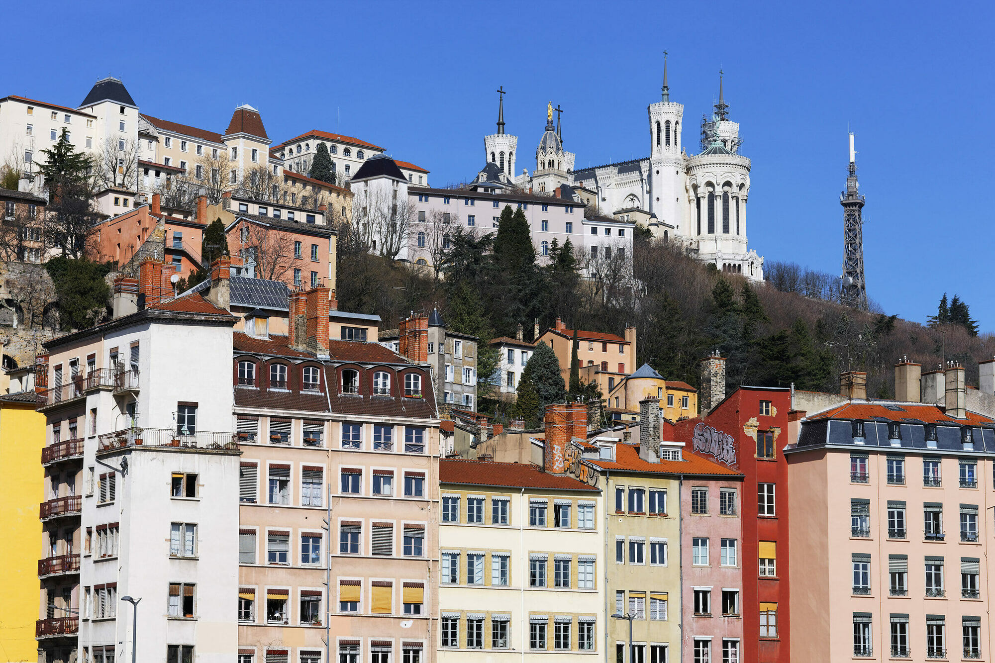 Façades colorées des quais de Saône à Lyon, dominées par la colline de Fourvière, sa basilique et sa tour métallique