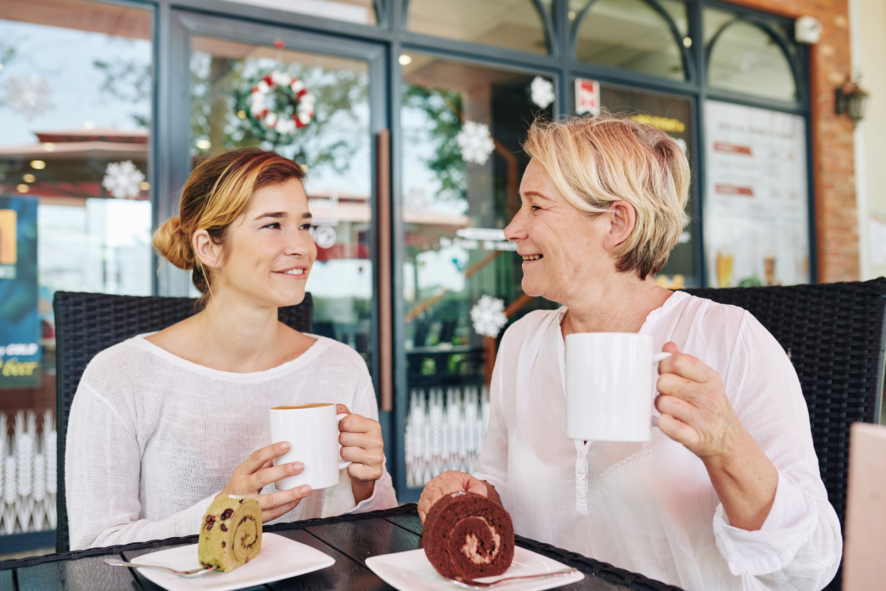 Une mère aux cheveux blonds courts et sa fille partagent un café et des gâteaux roulés en terrasse