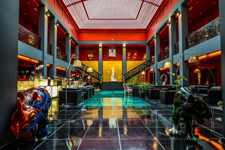 Hall d'hôtel au décor Art déco avec sol carrelé, balcons colorés sur plusieurs étages et verrière lumineuse