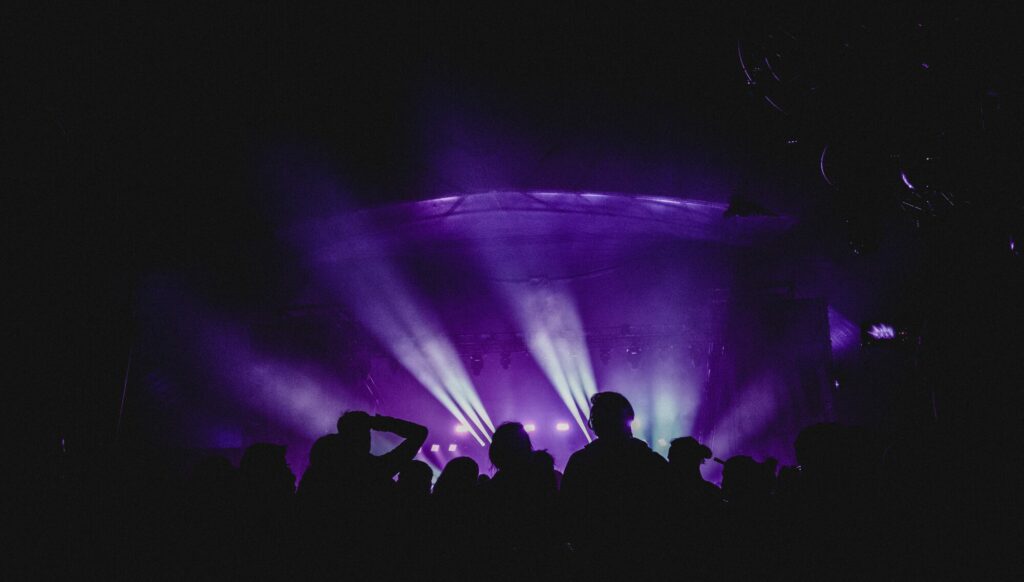 Silhouettes d’un public devant une scène de concert baignée de faisceaux lumineux violets
