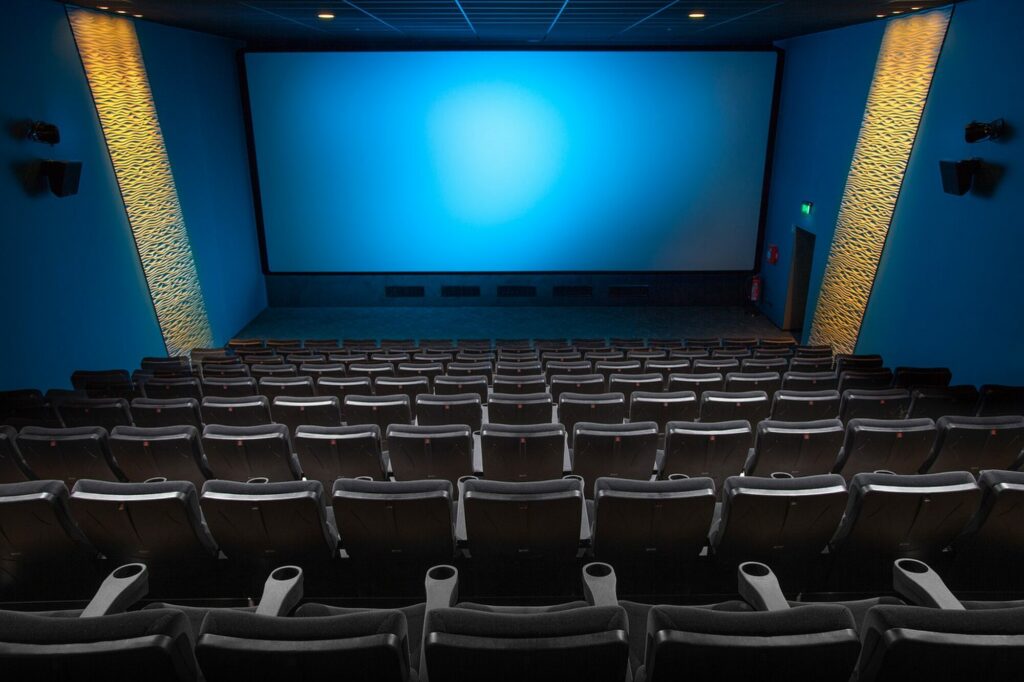 Salle de cinéma vide aux rangées de fauteuils sombres face à un grand écran bleu éclairé