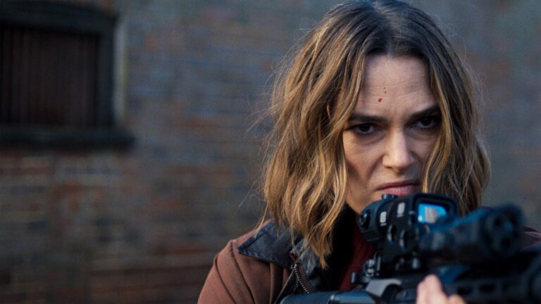 Keira Knightley, une arme à la main et le regard concentré, devant un mur de briques dans la saison 2 de la série Black Doves