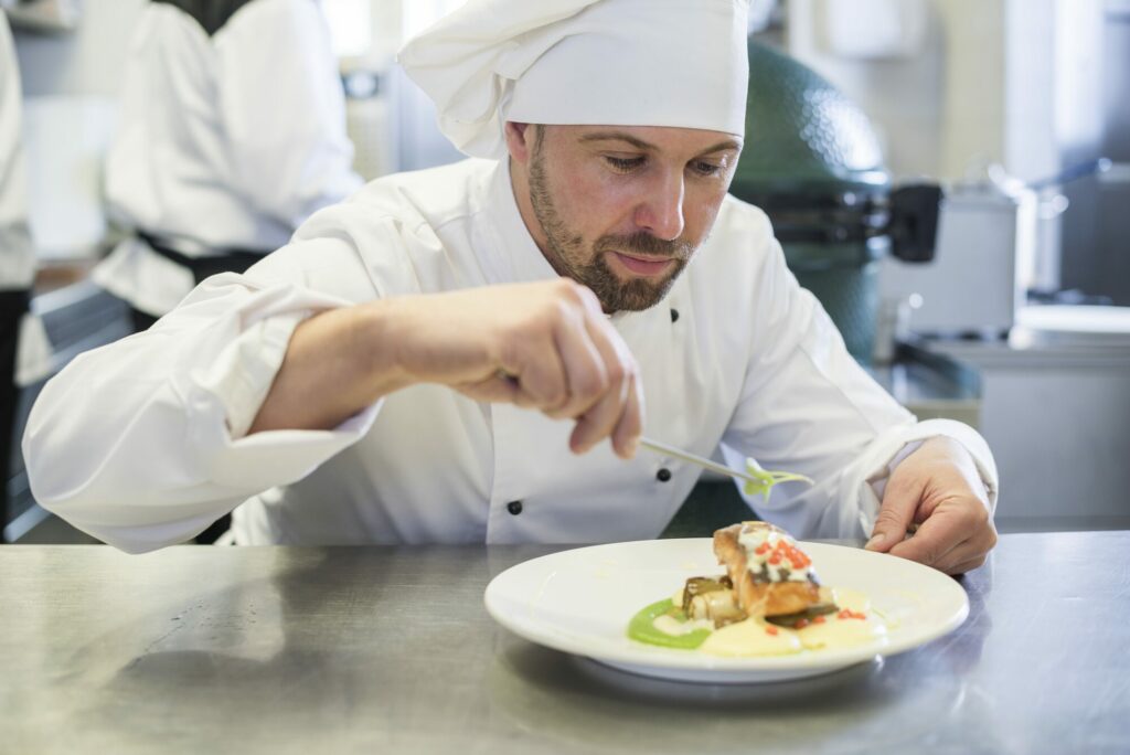 Un chef en veste et toque blanches dresse avec soin une assiette dans une cuisine professionnelle