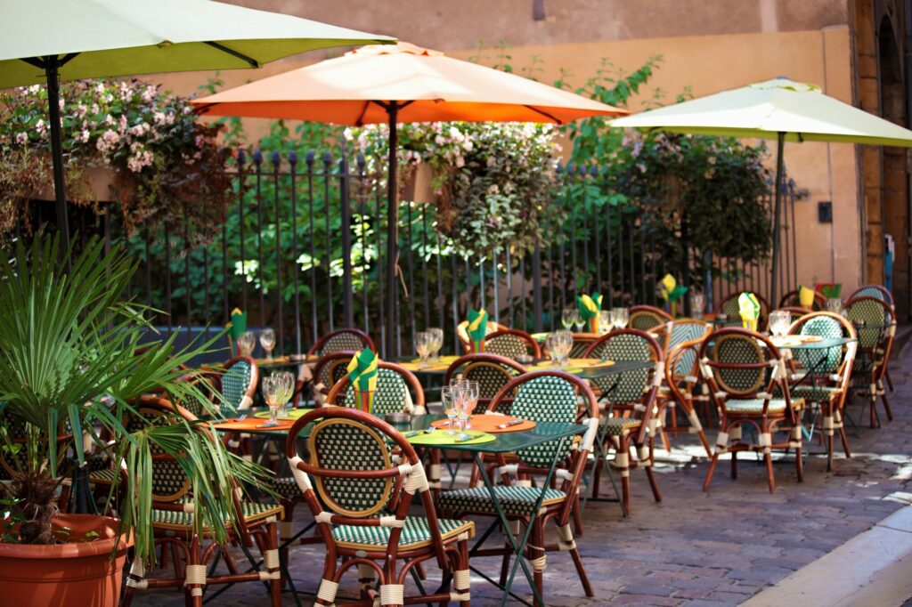 Terrasse de restaurant avec chaises bistrot tressées, tables dressées et parasols orange et verts