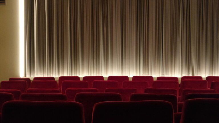Salle de cinéma vide aux fauteuils rouges face à un rideau fermé éclairé