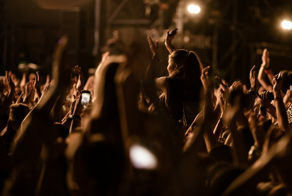 Public d’un concert les bras levés, en contre-jour devant les lumières de la scène