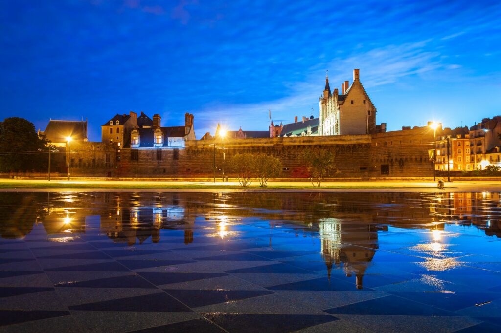 Le château des ducs de Bretagne à Nantes illuminé à l'heure bleue, reflété dans le miroir d'eau au premier plan
