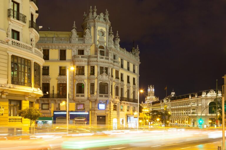 Immeubles illuminés de la Gran Vía à Madrid la nuit, avec des traînées lumineuses de voitures