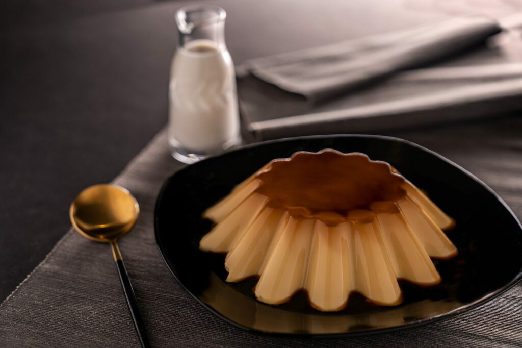 Flan au caramel nappé de sauce dans une assiette sombre, à côté d'une petite bouteille de lait