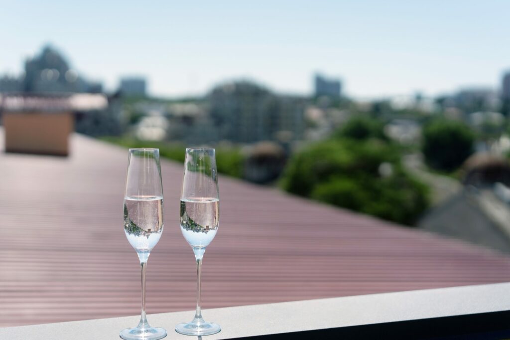 Deux coupes de champagne posées sur un rebord de toit, face aux toits et aux arbres d’une ville