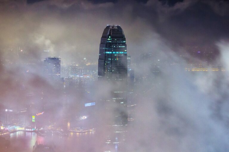 Gratte-ciel illuminés émergeant d'un épais brouillard nocturne au-dessus d'une mégalopole