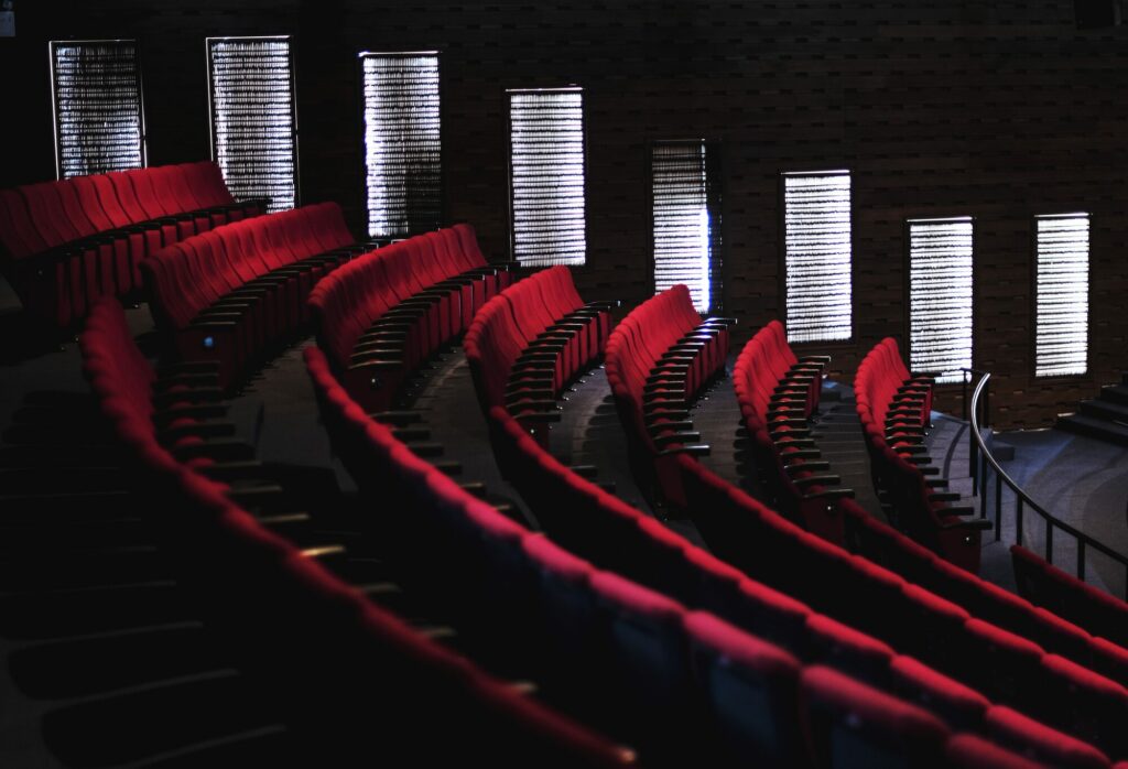 Rangées incurvées de fauteuils rouges vides dans une salle de spectacle plongée dans la pénombre