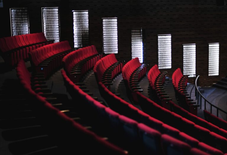 Rangées incurvées de fauteuils rouges vides dans une salle de spectacle plongée dans la pénombre