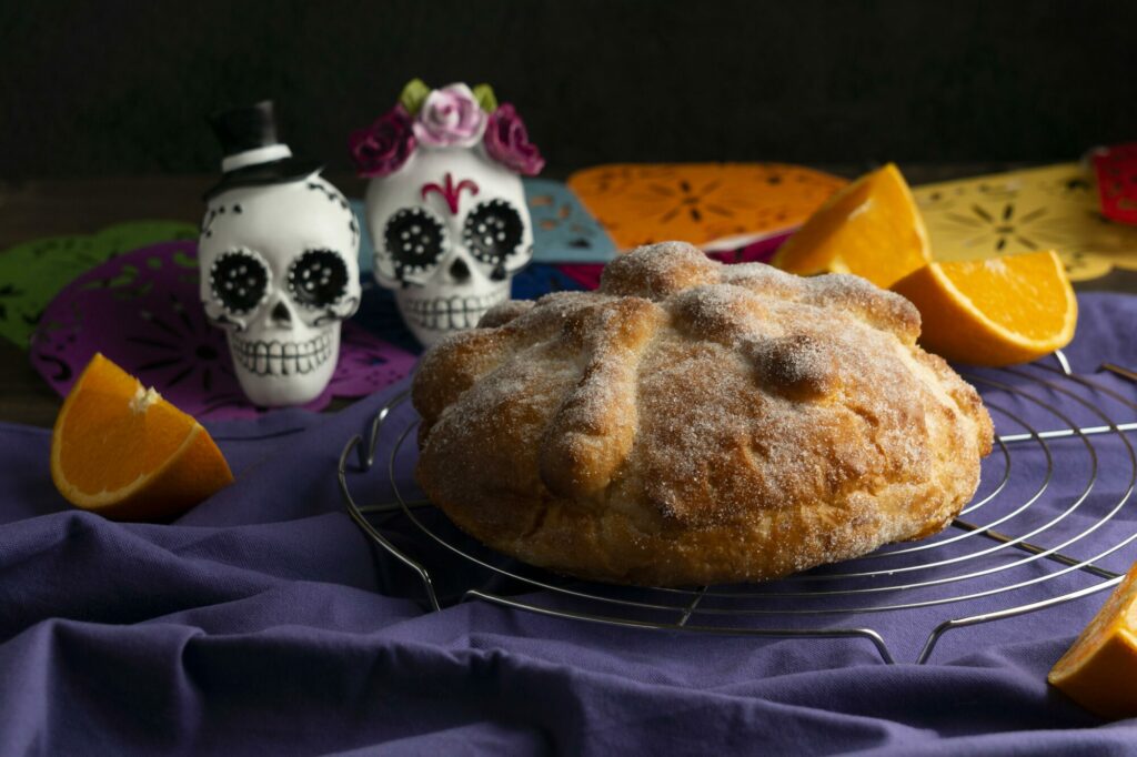 Pain des morts mexicain entouré de crânes en sucre décorés et de pétales orangés sur une nappe violette