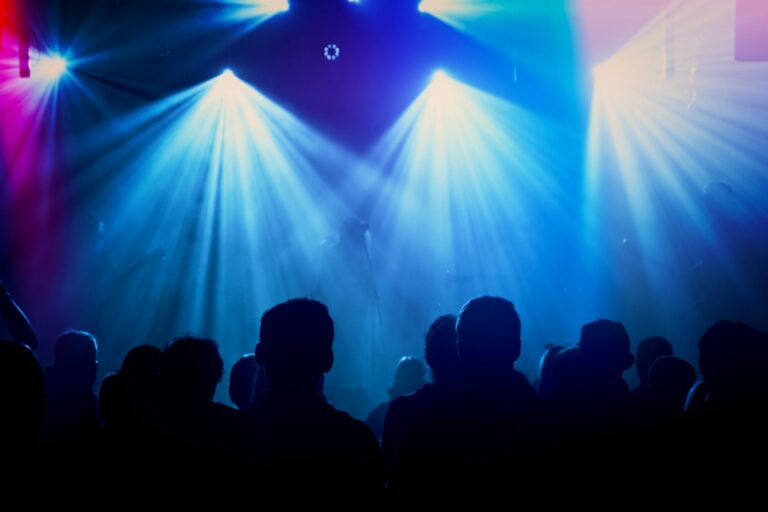 Silhouettes du public devant une scène de concert baignée de faisceaux lumineux bleus et violets