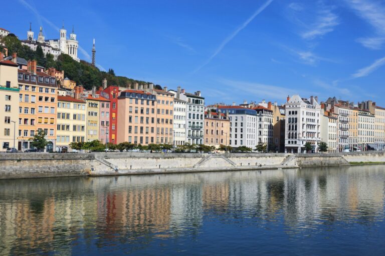 Façades colorées des quais de Saône à Lyon sous un ciel bleu, avec la colline de Fourvière en arrière-plan