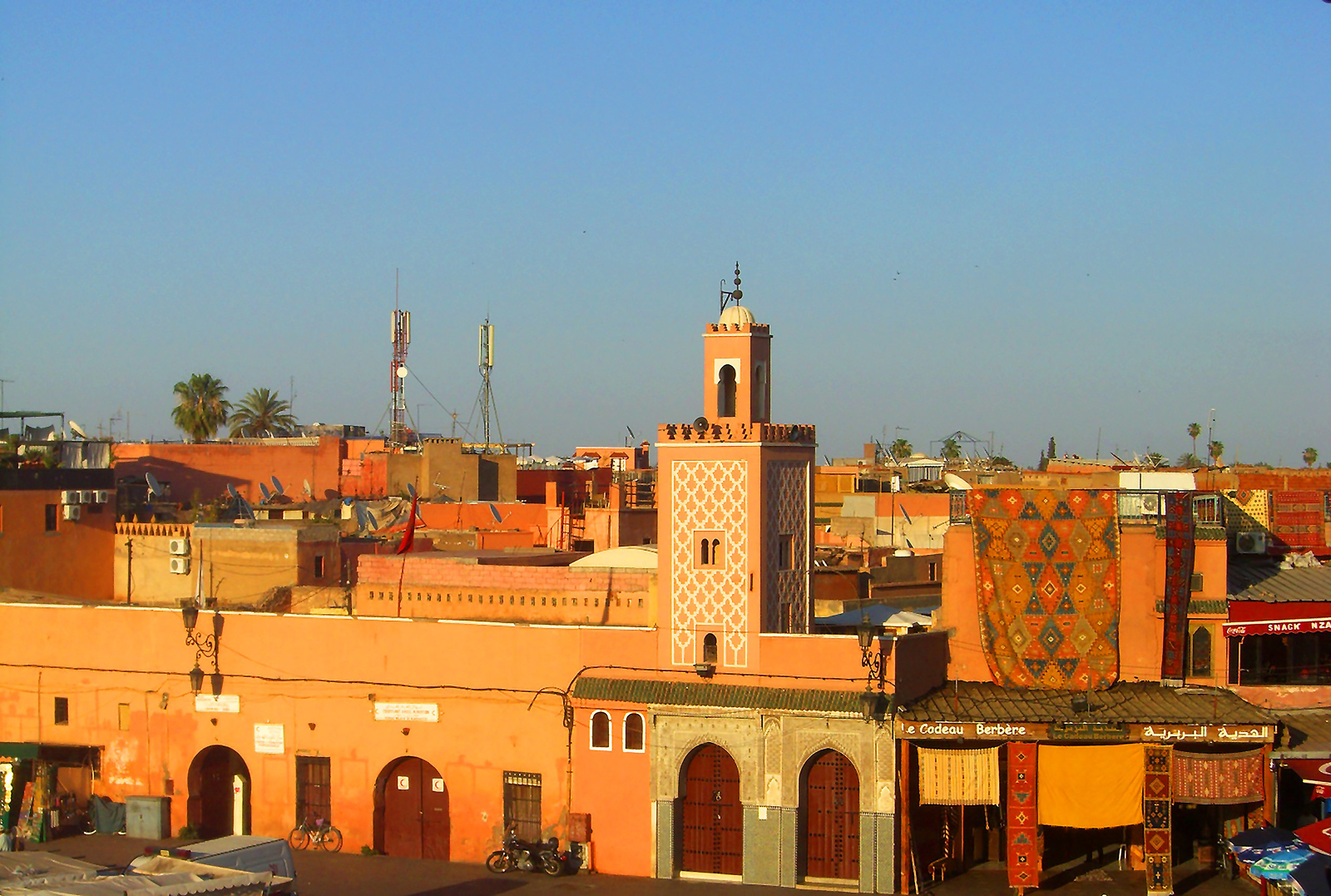 Façades ocre et minaret d'une place de Marrakech au soleil couchant