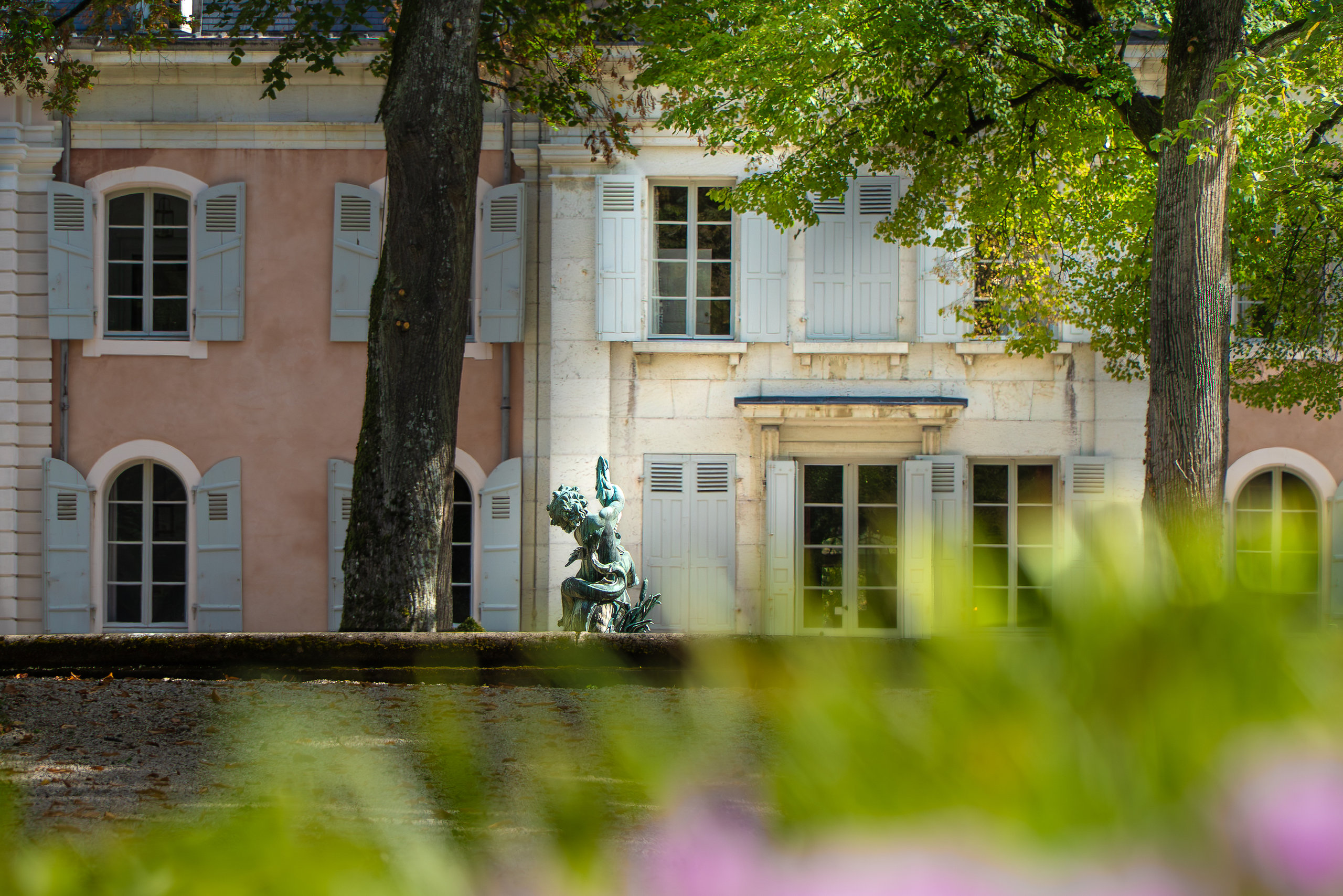 Façade rose aux volets gris-bleu du château de Voltaire, vue depuis les jardins
