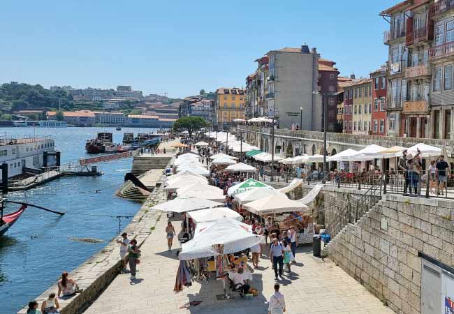 Terrasses animées et parasols sur les quais de la Ribeira à Porto, un jour d'été