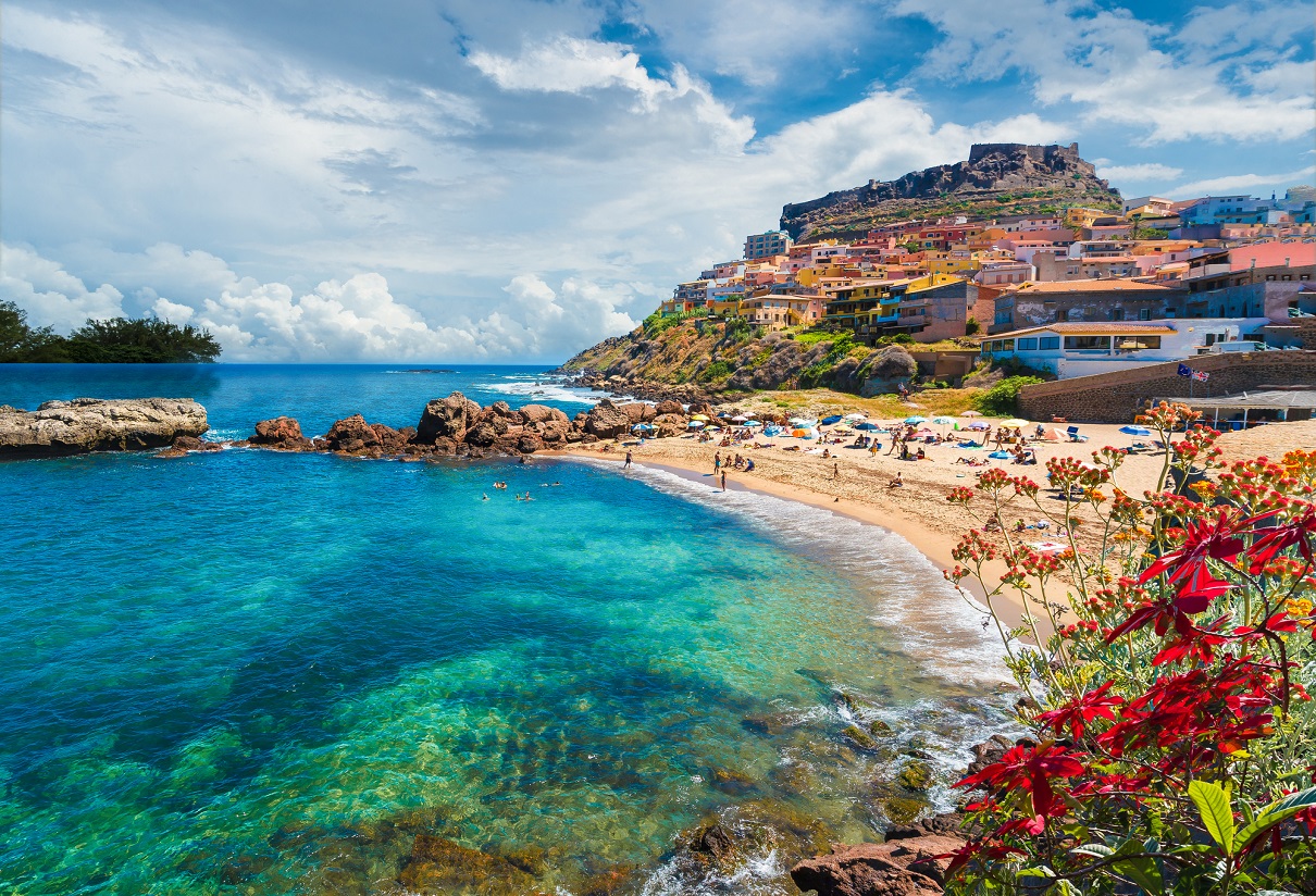 Plage de sable, rochers et village perché aux maisons colorées en Sardaigne