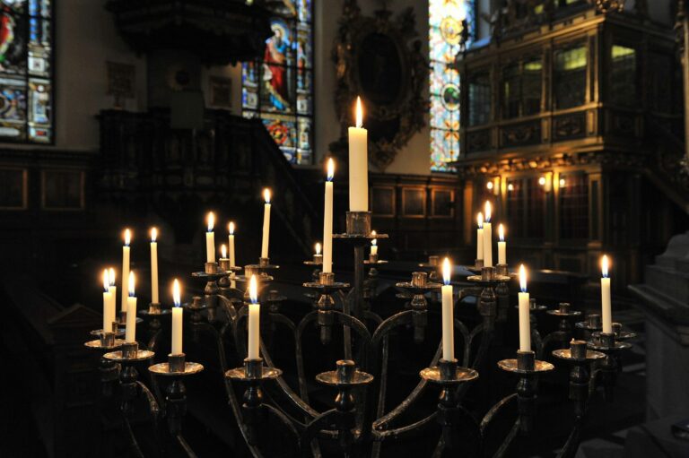 Grand chandelier aux bougies allumées dans la pénombre d’une église aux vitraux sombres