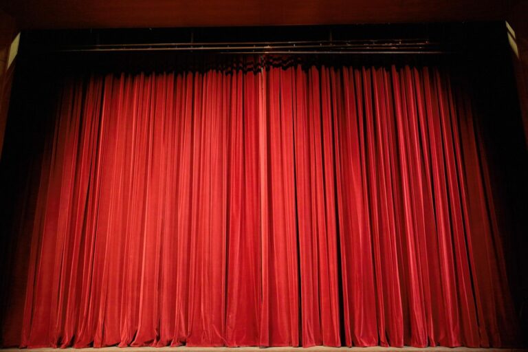 Rideau de scène en velours rouge fermé dans une salle de théâtre plongée dans la pénombre