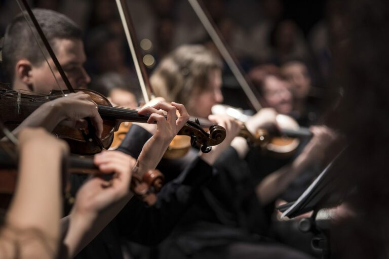 Violonistes d’un orchestre en plein concert, archets levés dans une lumière chaude et tamisée