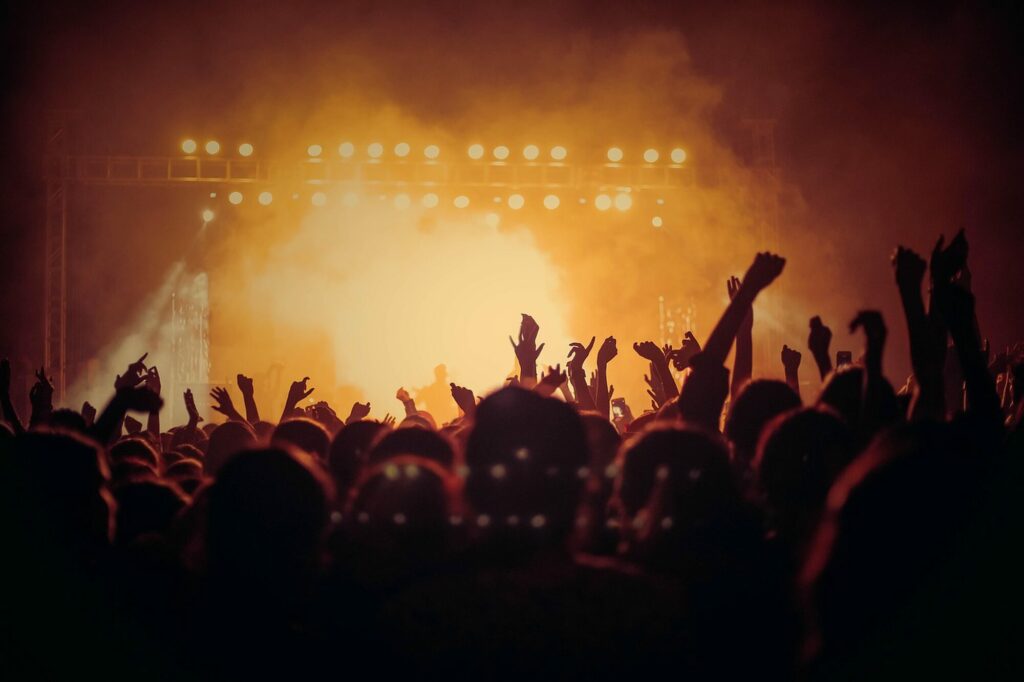 Silhouettes d'un public bras levés devant une scène de concert baignée de lumière orangée