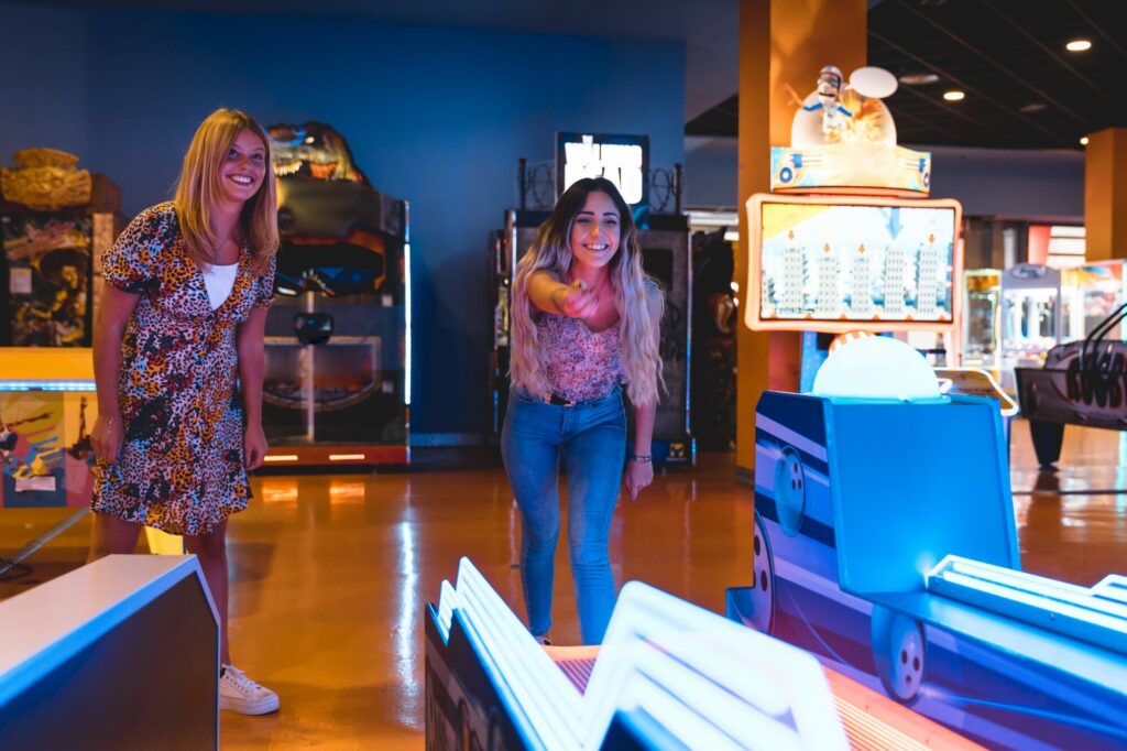 Deux jeunes femmes jouant à une borne d’arcade dans une salle de jeux éclairée de lumières bleues
