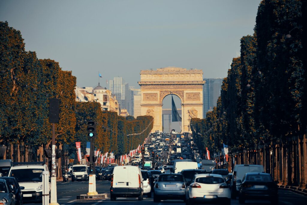 Avenue des Champs-Élysées bordée d’arbres et animée de voitures, avec l’Arc de triomphe au fond
