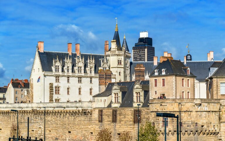 Le château des ducs de Bretagne à Nantes, avec la tour Bretagne en arrière-plan, sous un ciel bleu nuageux