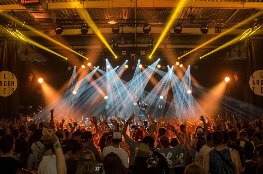 Public d'un concert face à une scène baignée de faisceaux lumineux blancs et bleus