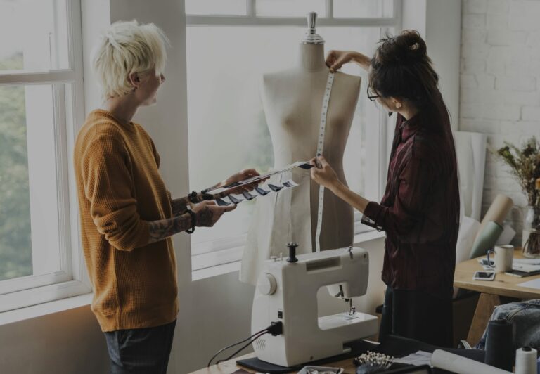 Deux couturières dans un atelier lumineux, l'une prenant des mesures sur un mannequin de couture près d'une machine à coudre
