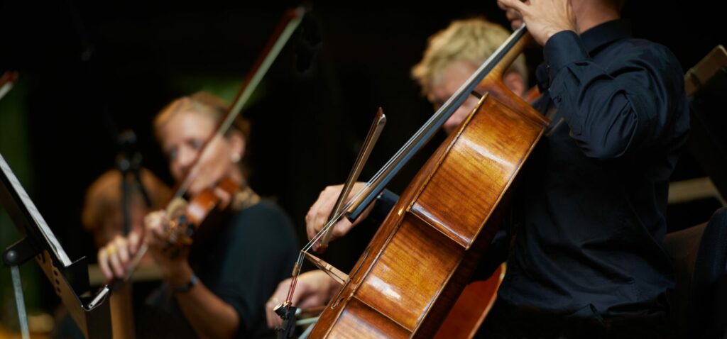 Musiciens d’orchestre jouant du violoncelle et du violon sur une scène plongée dans la pénombre