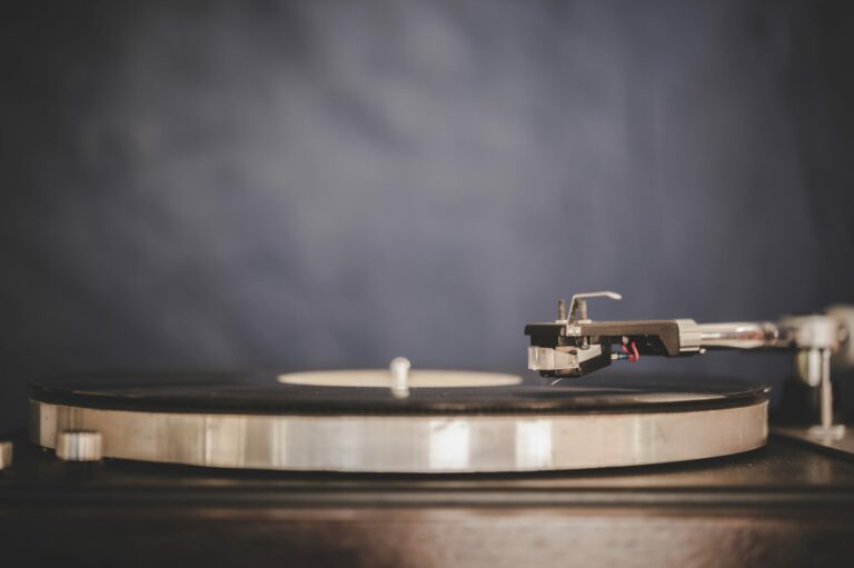 Platine vinyle argentée avec un disque noir posé sur le plateau, sur fond gris sombre