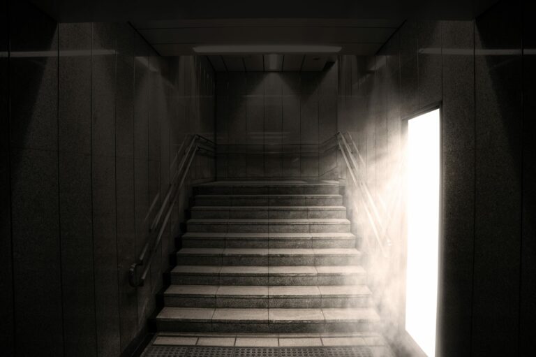 Escalier plongé dans l’obscurité, éclairé sur le côté par la lumière d’une porte entrouverte