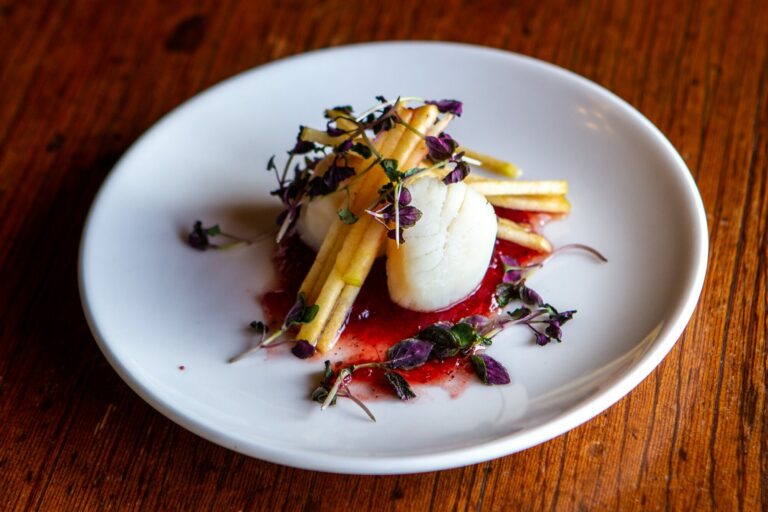 Assiette gastronomique de saint-jacques et de légumes dressée sur une assiette blanche posée sur une table en bois